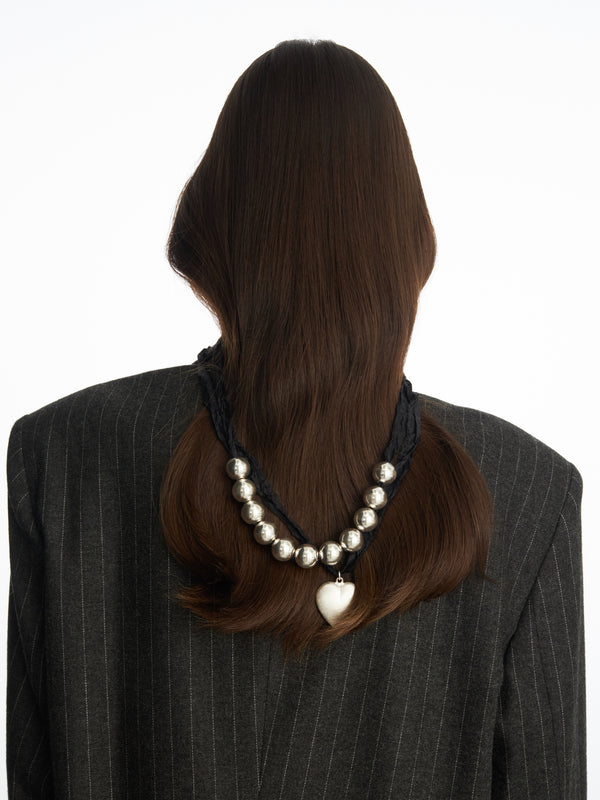 Stylizacja długiego naszyjnika na czarnej wstążce ze srebrnymi elementami