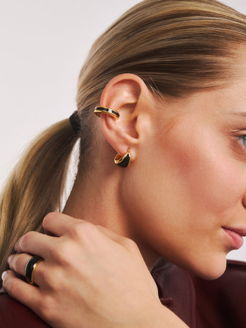  Cienka pozłacana nausznica z czarną emalią z kolekcji Viva na jednym uchu z pozłacanym kolczykiem z czarną emalią 