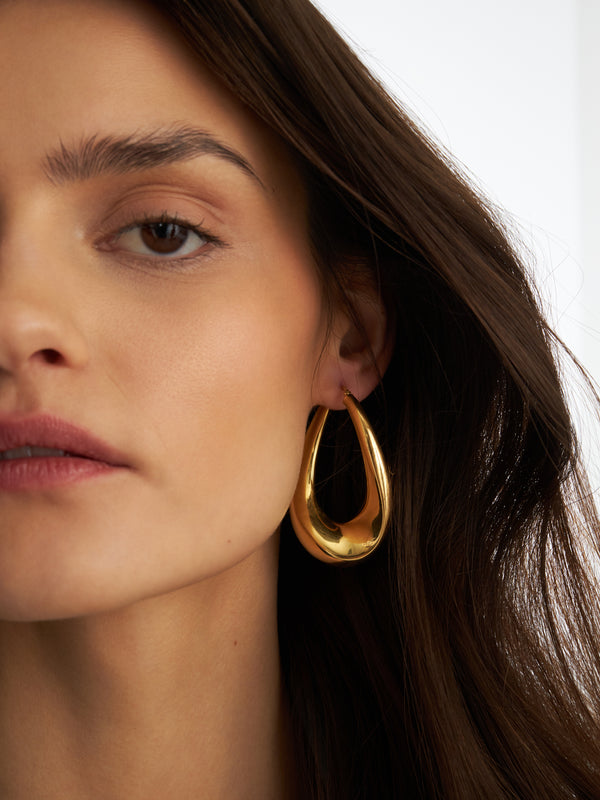 Duże pozłacane kolczyki zawijane w kształcie wydłużonej pętli, wykonane ze srebra 925 pokrytego 18-karatowym złotem, prezentowane na uchu modelki.